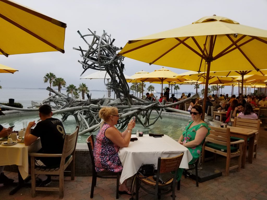 Seaside cafe seating with umbrellas and modern art fountain sculpture