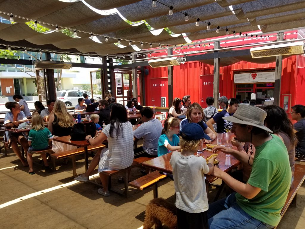 Families and diners of all ages eat at picnic tables under a cloth ceiling at SteelCraft